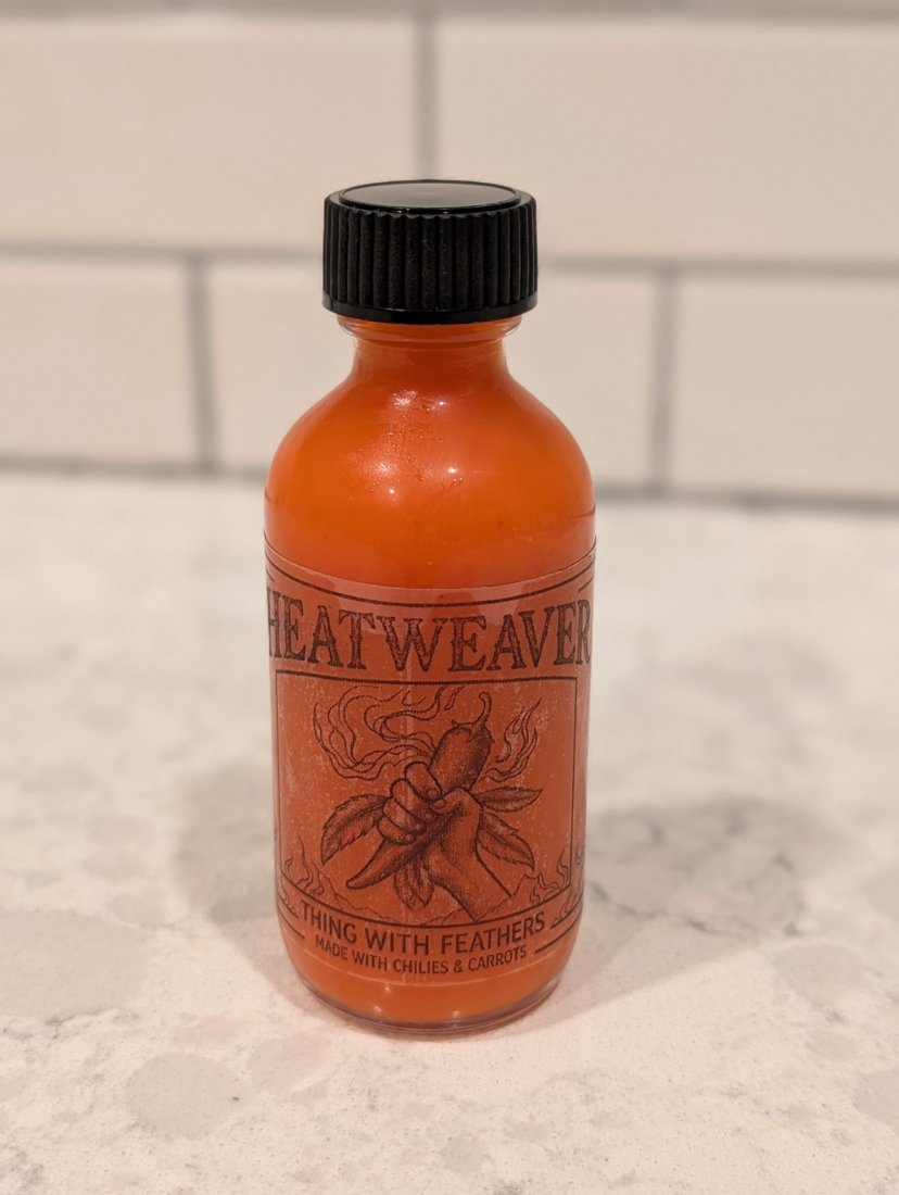 A 2 oz bottle of Heatweaver Thing With Feathers hot sauce on a marble counter